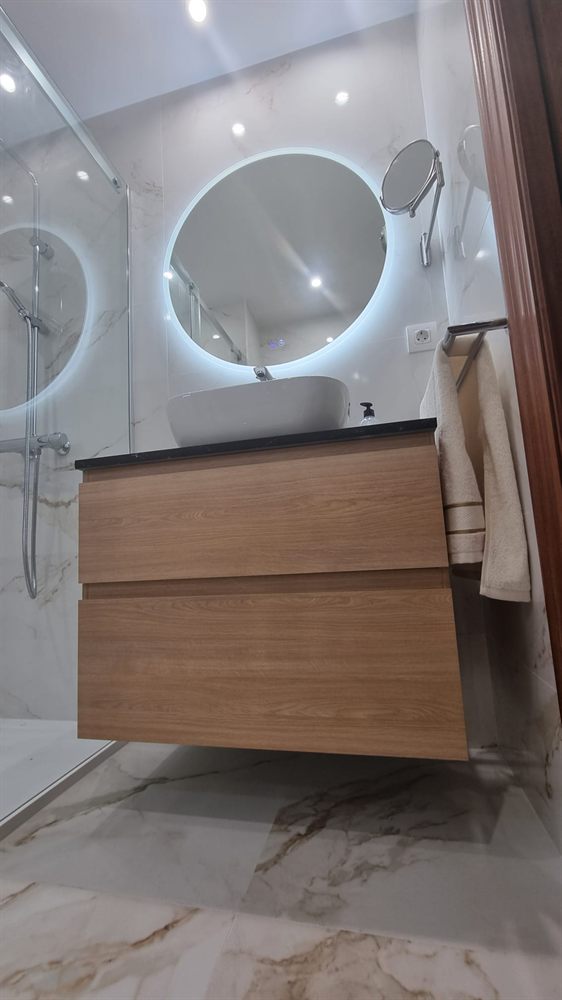 Baño con mueble de madera y espejo redondo retroiluminado