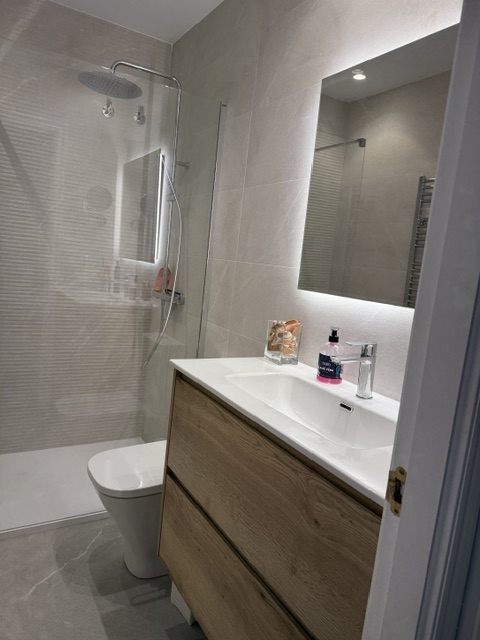 Baño con lavabo sobre mueble de madera y espejo con luz