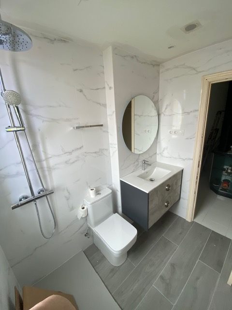Baño con mueble azul, espejo redondo y ducha
