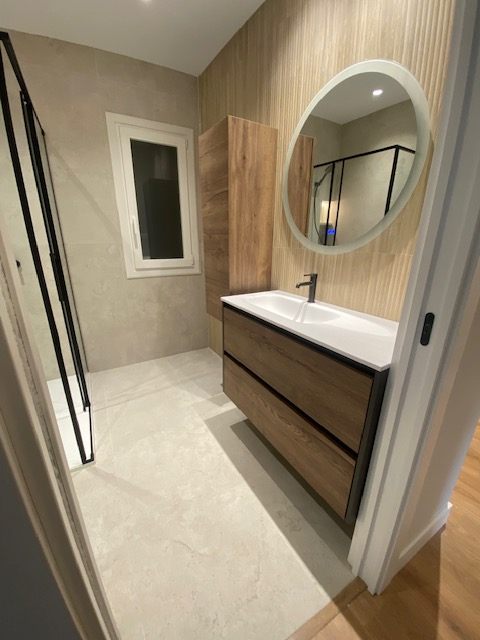 Baño con mueble de madera, espejo redondo y ventana