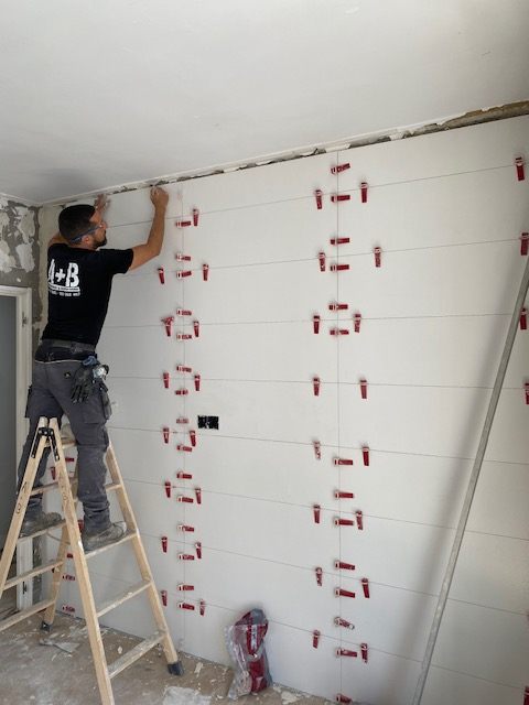 Operario de Proyectos y Reformas A+B alicatando una pared subido a una escalera